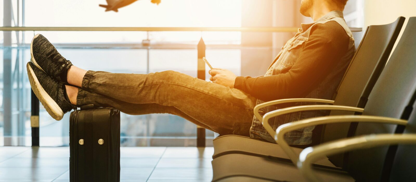 Traveler relaxes at airport while waiting for flight boarding, with plane taking off in background.