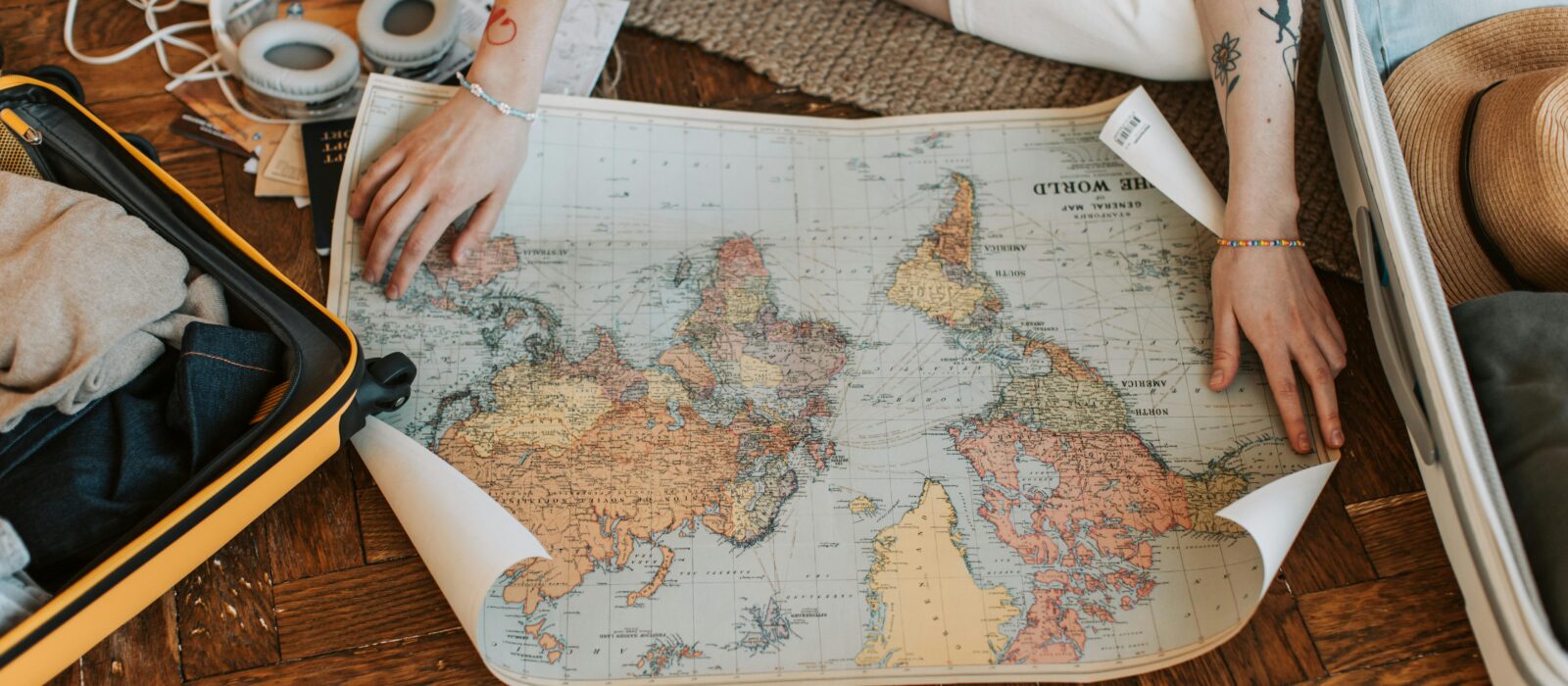 A traveler plans a journey, sitting on the floor with a world map and suitcase filled with essentials.